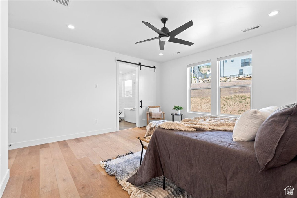 Bedroom featuring a barn door, light wood finished floors, connected bathroom, recessed lighting, and ceiling fan