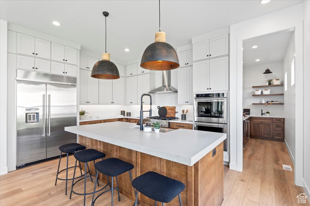 Kitchen with appliances with stainless steel finishes, light countertops, light wood-type flooring, recessed lighting, and a kitchen island with sink