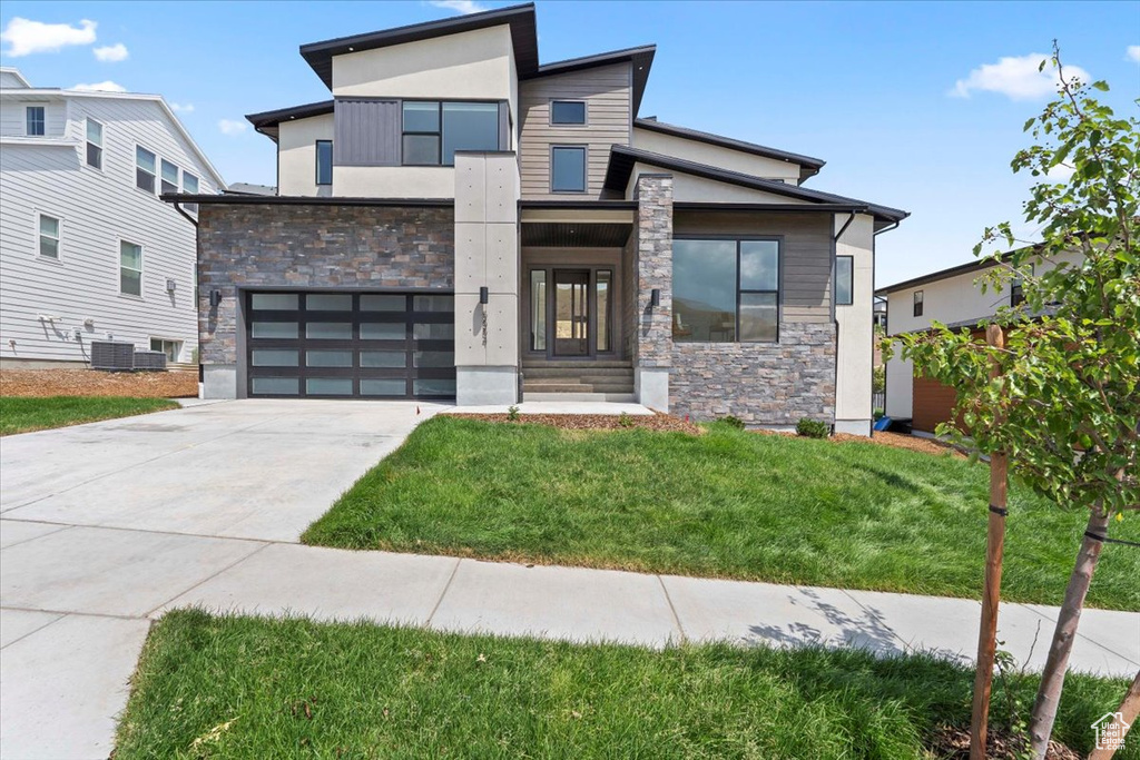 Contemporary home featuring stone siding, concrete driveway, an attached garage, and a front yard
