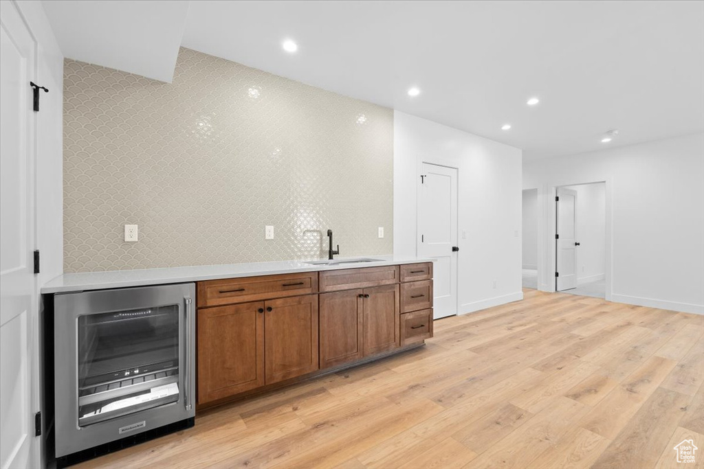 Bar with wine cooler, light wood-style floors, recessed lighting, and tasteful backsplash