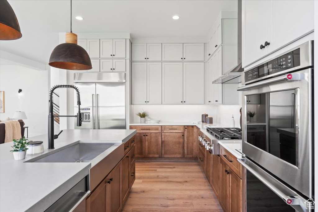 Kitchen with appliances with stainless steel finishes, light wood-type flooring, light countertops, brown cabinets, and recessed lighting