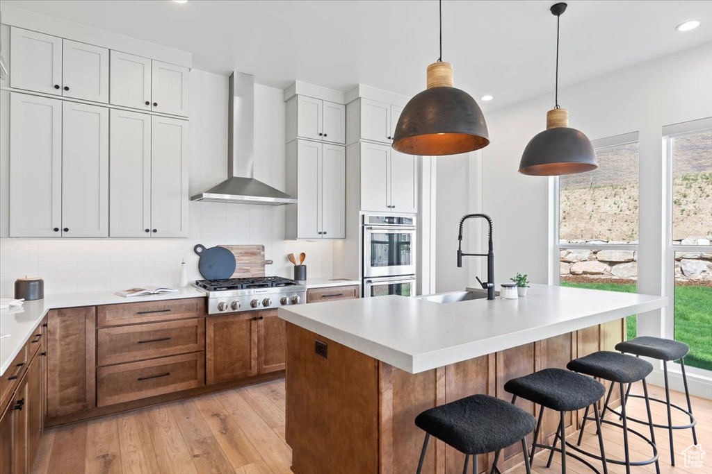 Kitchen featuring wall chimney exhaust hood, appliances with stainless steel finishes, light wood-style floors, tasteful backsplash, and recessed lighting
