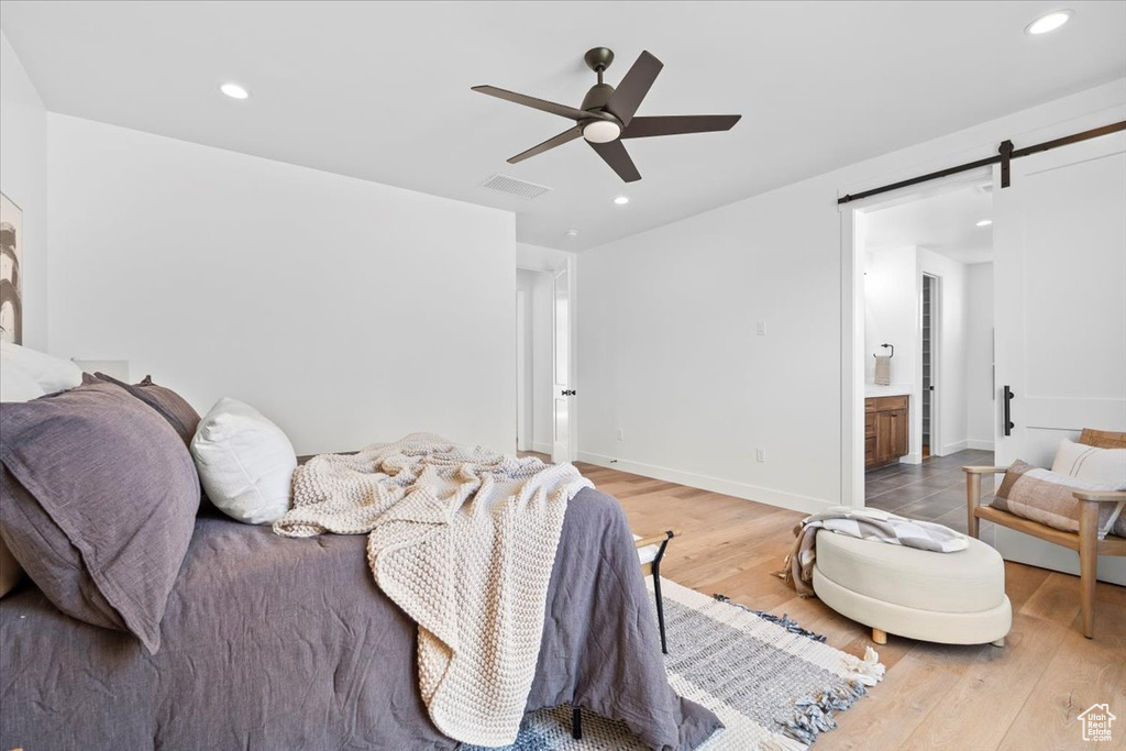 Bedroom with a barn door, light wood finished floors, recessed lighting, ceiling fan, and ensuite bath