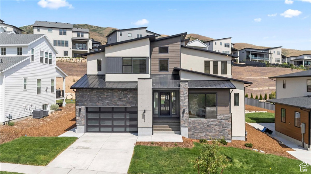 Contemporary house featuring stone siding, a standing seam roof, a residential view, a garage, and concrete driveway