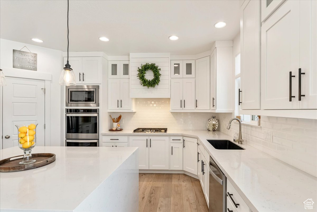 Kitchen featuring appliances with stainless steel finishes, white cabinetry, glass insert cabinets, light stone counters, and recessed lighting