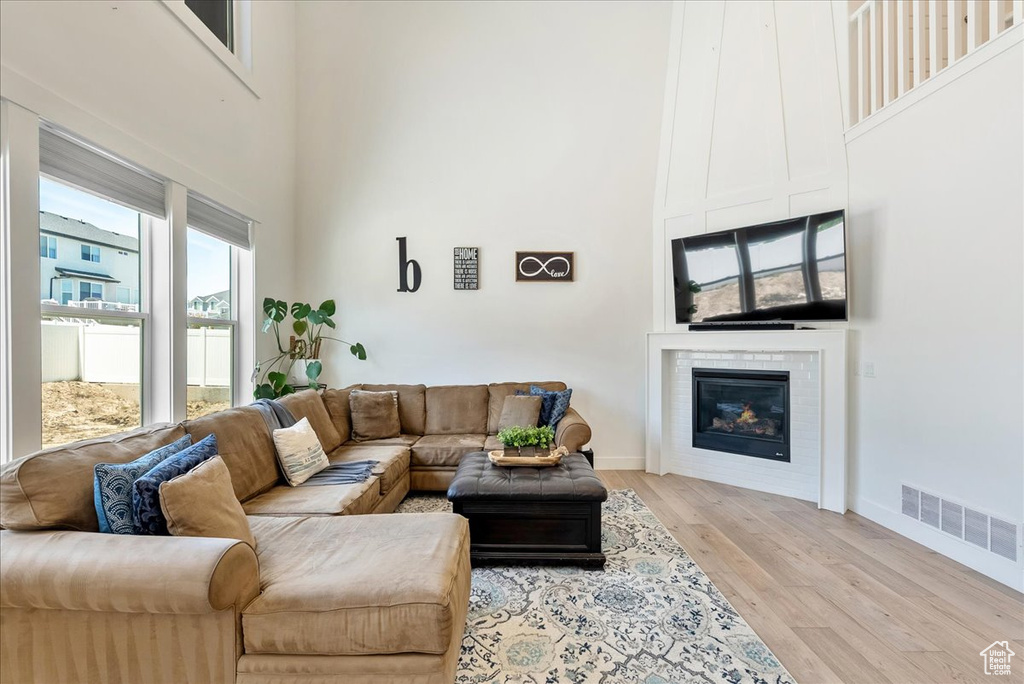 Living area featuring a high ceiling, light wood-type flooring, and a glass covered fireplace