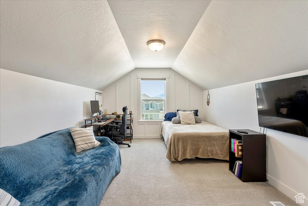 Bedroom with vaulted ceiling, a textured ceiling, and light colored carpet