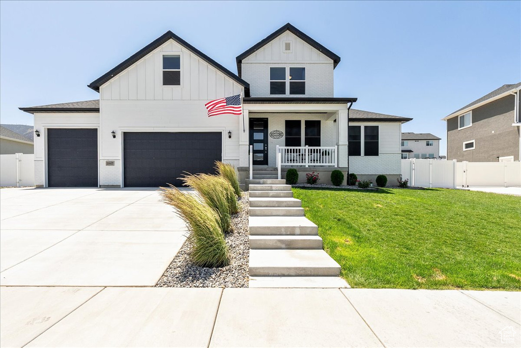 View of front facade featuring board and batten siding, covered porch, driveway, and a garage