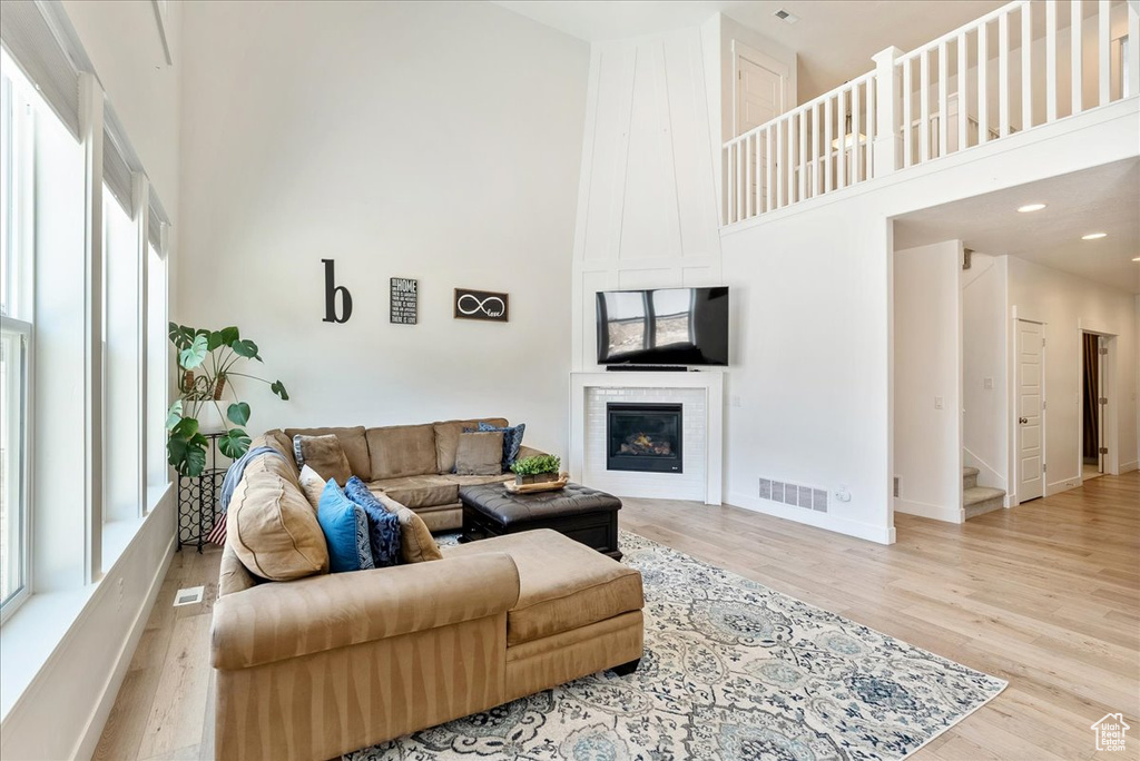 Living area featuring a high ceiling, light wood-type flooring, a glass covered fireplace, stairs, and recessed lighting