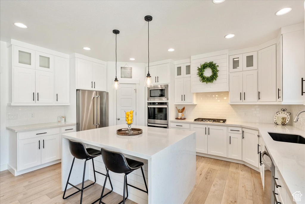 Kitchen featuring appliances with stainless steel finishes, a kitchen island, a breakfast bar, light wood-type flooring, and recessed lighting