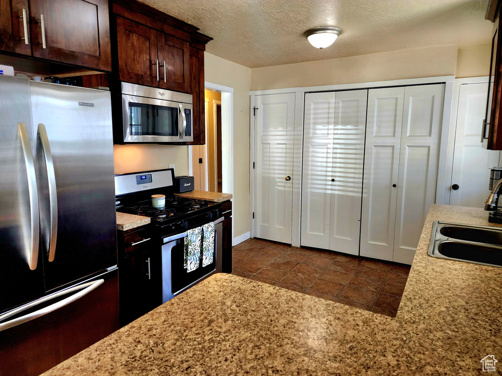 Kitchen featuring appliances with stainless steel finishes, dark brown cabinets, and a textured ceiling