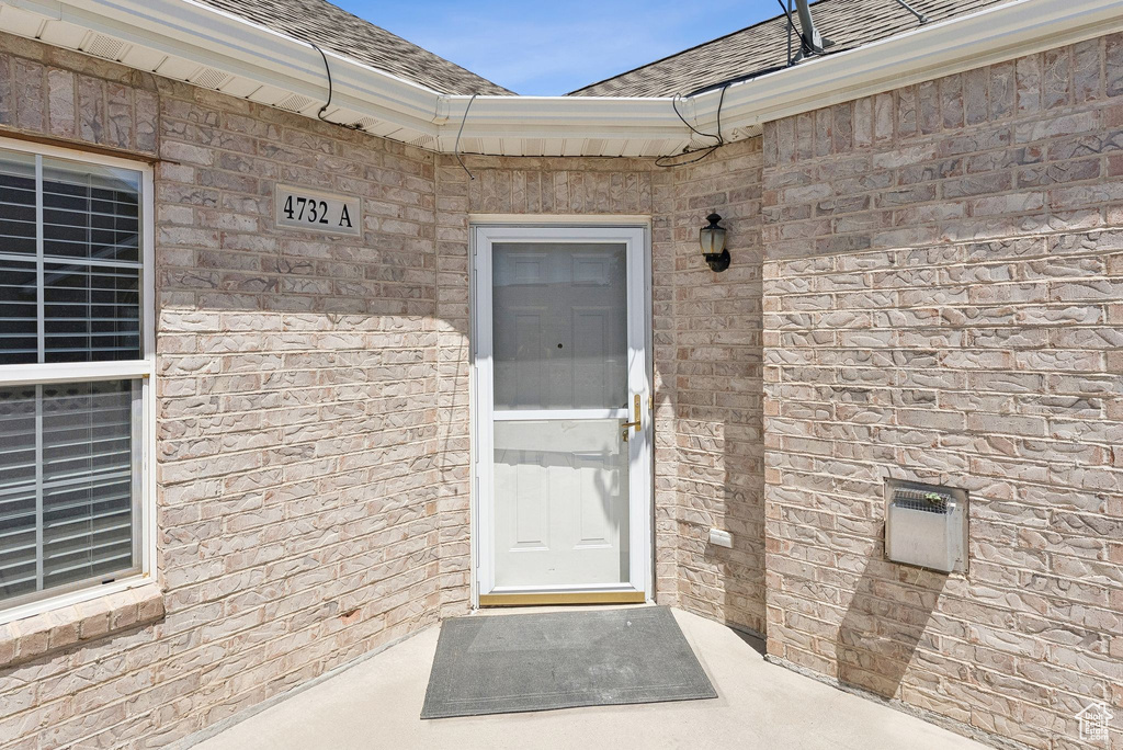 Property entrance featuring a shingled roof and brick siding