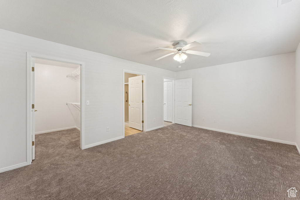 Unfurnished bedroom featuring carpet floors, a spacious closet, a ceiling fan, and a closet