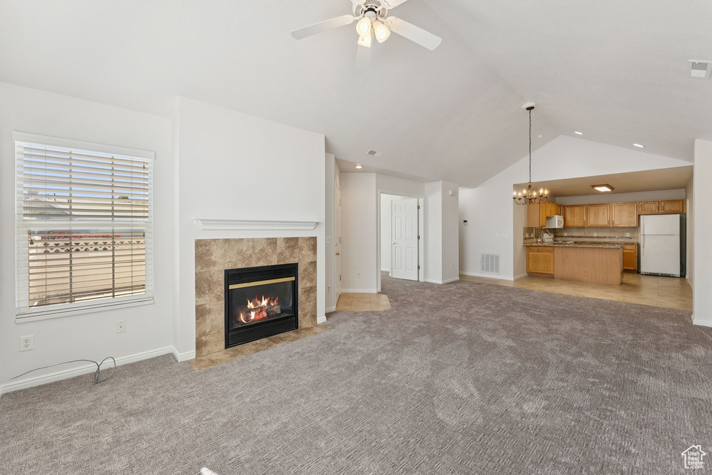 Unfurnished living room featuring a tile fireplace, lofted ceiling, a chandelier, a ceiling fan, and light colored carpet