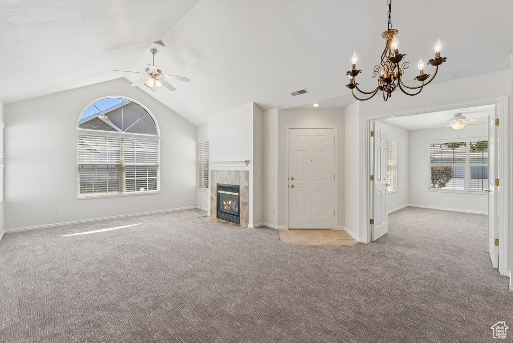 Unfurnished living room featuring a ceiling fan, light carpet, lofted ceiling, a fireplace, and a chandelier