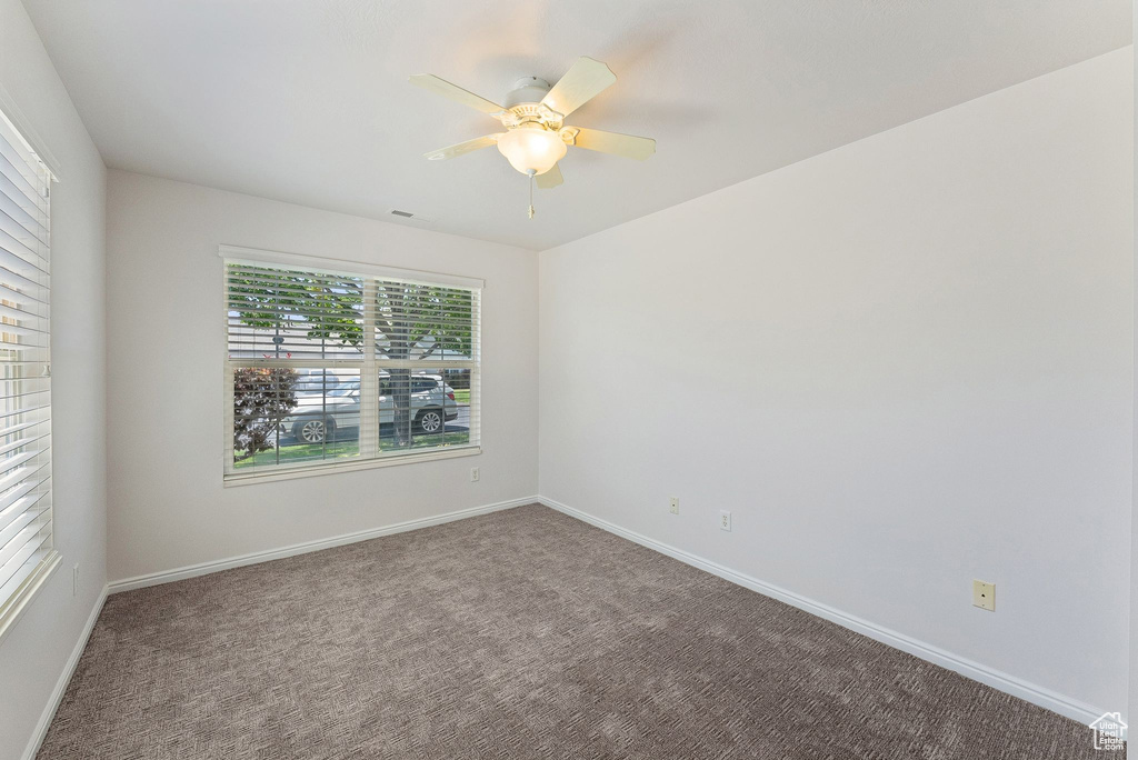 Carpeted spare room featuring ceiling fan and baseboards
