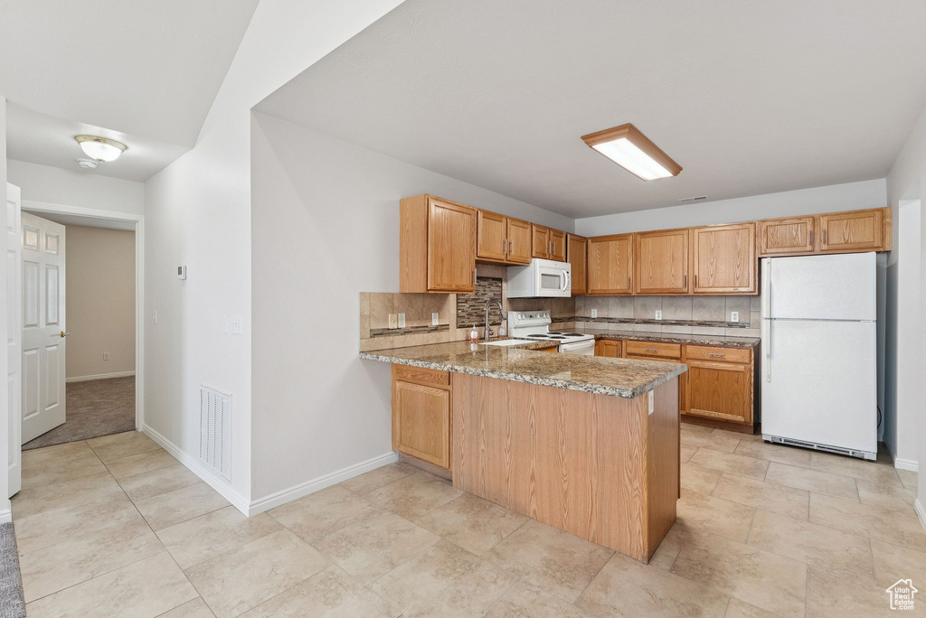 Kitchen with white appliances, backsplash, a peninsula, and light stone counters