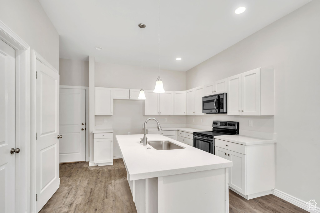 Kitchen featuring appliances with stainless steel finishes, light wood finished floors, white cabinets, an island with sink, and pendant lighting