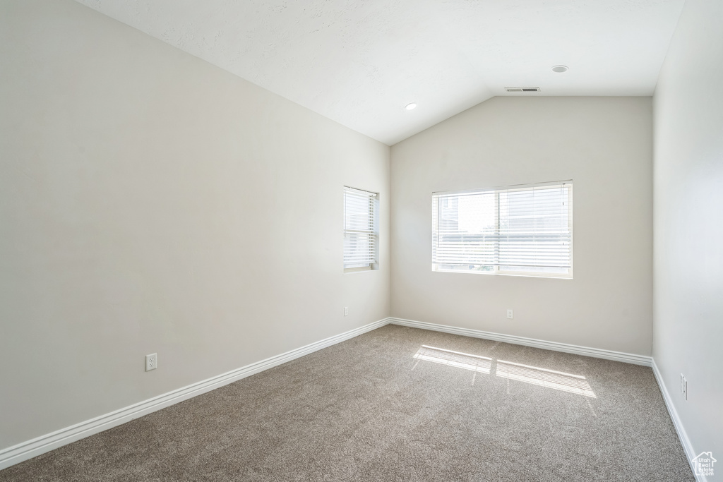 Carpeted spare room featuring lofted ceiling and baseboards