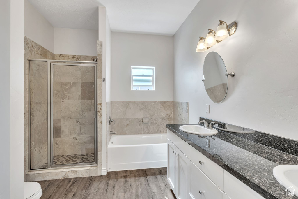 Bathroom with double vanity, a stall shower, a bath, and wood finished floors