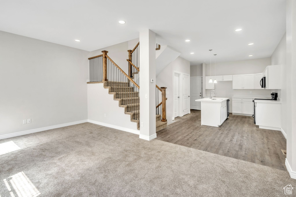 Kitchen featuring light carpet, open floor plan, a center island with sink, white cabinets, and recessed lighting