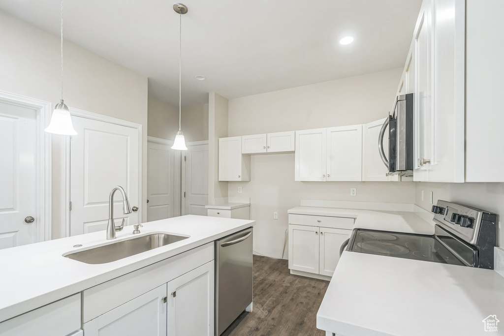 Kitchen with stainless steel appliances, white cabinetry, pendant lighting, dark wood-style floors, and light countertops
