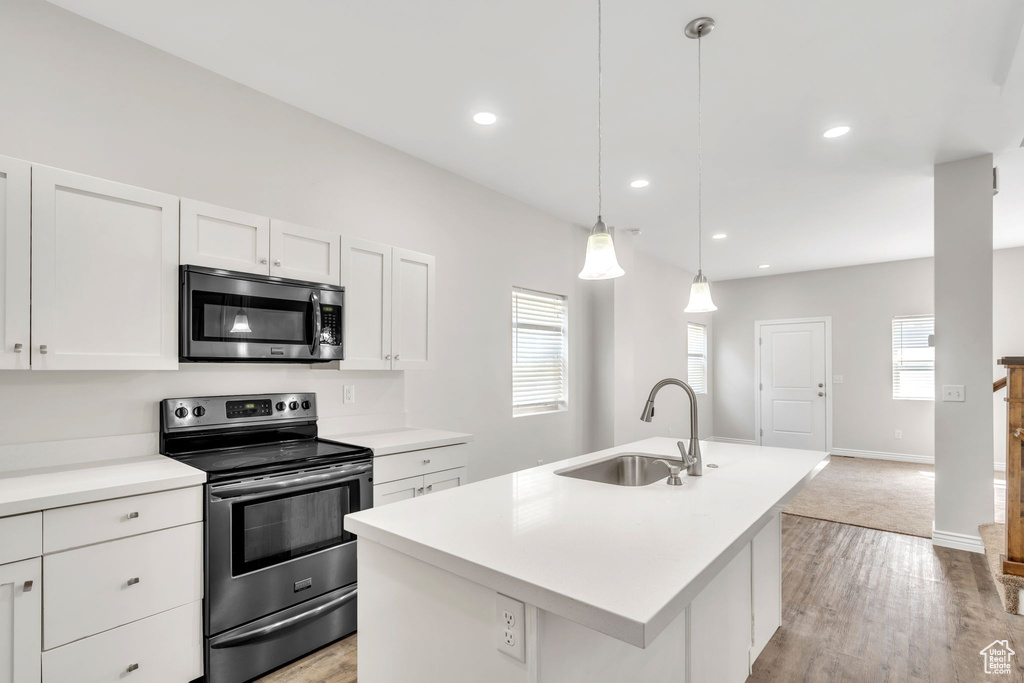Kitchen with appliances with stainless steel finishes, white cabinets, light countertops, a center island with sink, and light wood finished floors