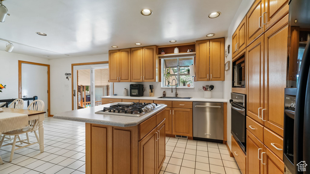 Kitchen featuring stainless steel appliances, light tile patterned flooring, light countertops, a kitchen island, and brown cabinetry