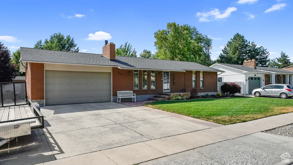 Ranch-style home with brick siding, a garage, a front lawn, a chimney, and concrete driveway