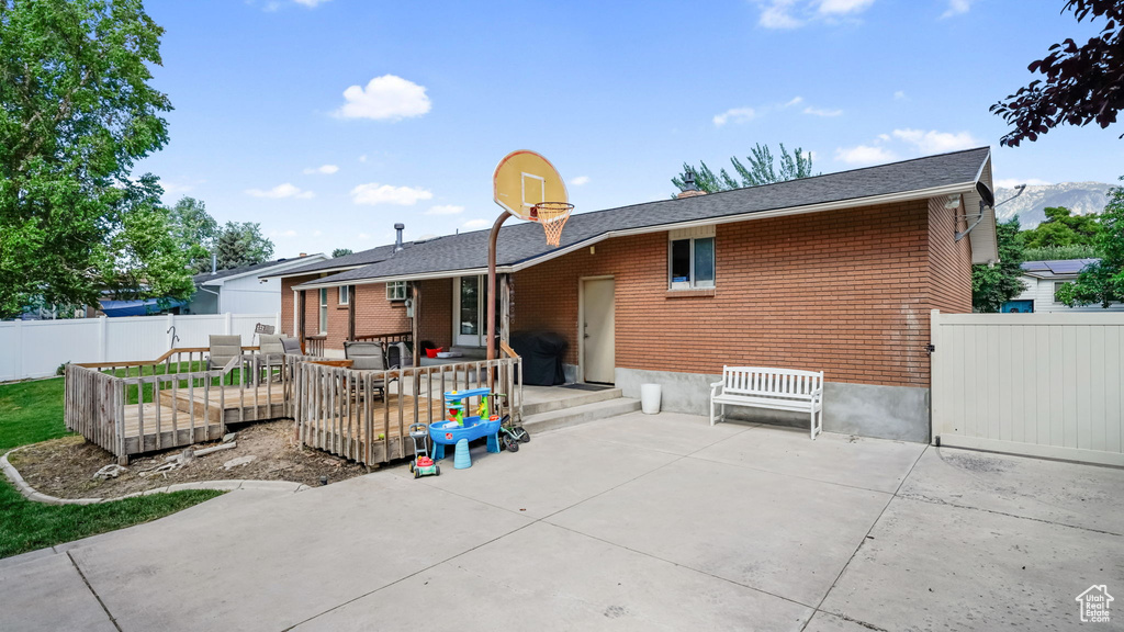 Back of property with a deck, brick siding, and a patio