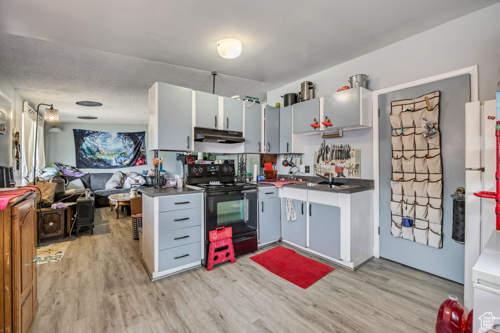 Kitchen with electric range, under cabinet range hood, light wood-style flooring, and open floor plan