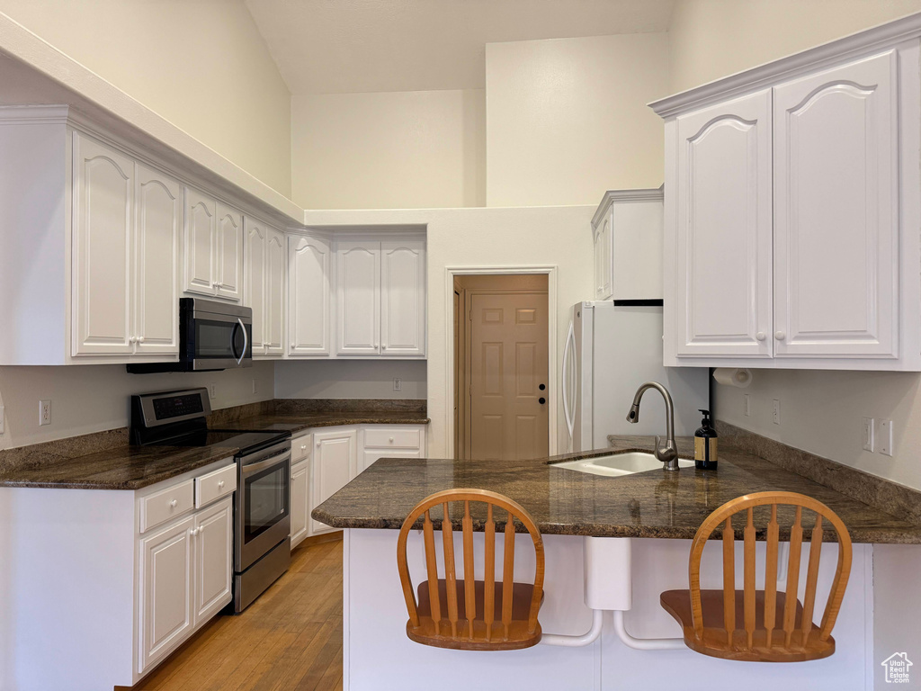 Kitchen with appliances with stainless steel finishes, a peninsula, light wood finished floors, and white cabinets