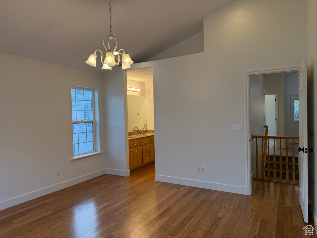 Spare room with dark wood-type flooring, a chandelier, and lofted ceiling
