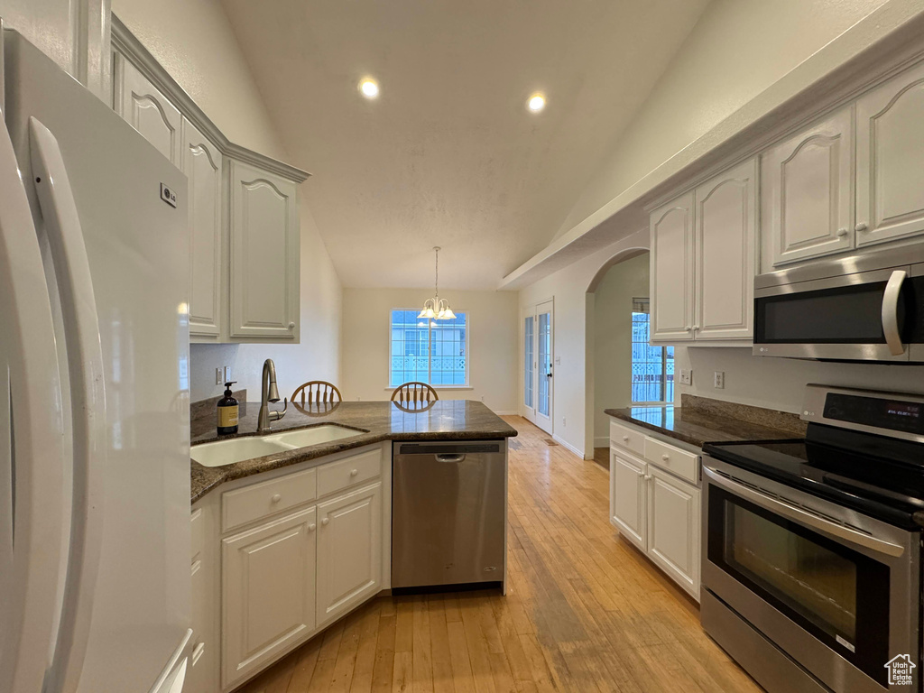 Kitchen featuring stainless steel appliances, lofted ceiling, recessed lighting, arched walkways, and dark stone countertops