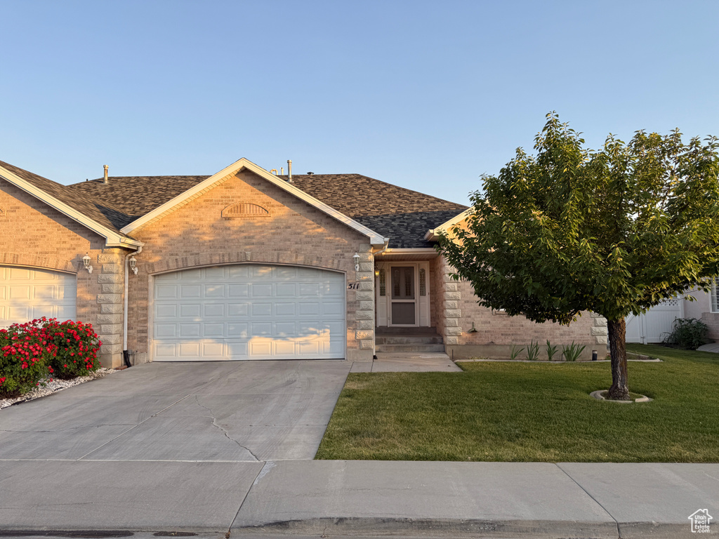 View of front of home featuring driveway, an attached garage, a front yard, roof with shingles, and brick siding