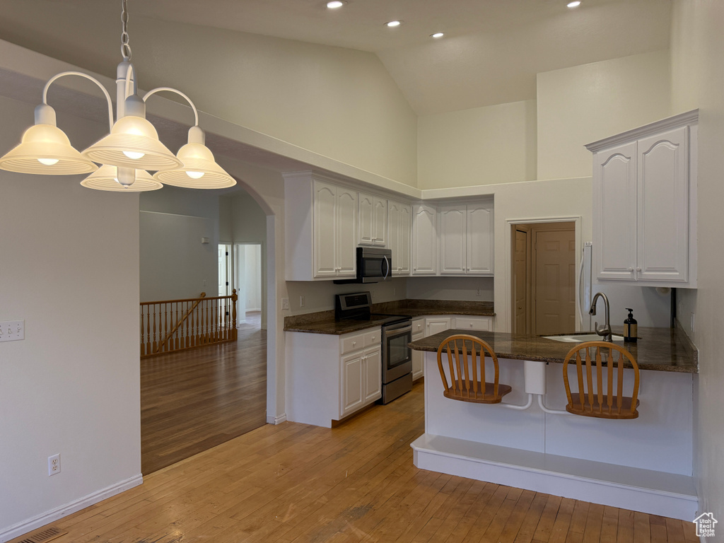 Kitchen featuring stainless steel appliances, high vaulted ceiling, a peninsula, light wood-style floors, and arched walkways