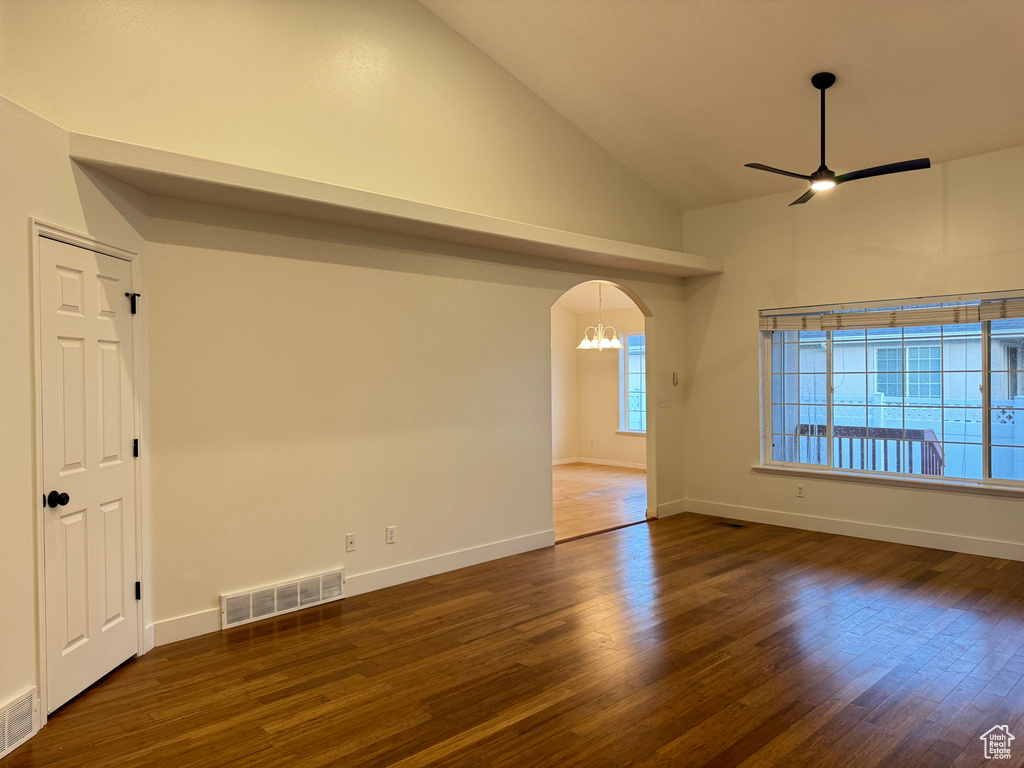Unfurnished room featuring a ceiling fan, wood finished floors, arched walkways, high vaulted ceiling, and a chandelier