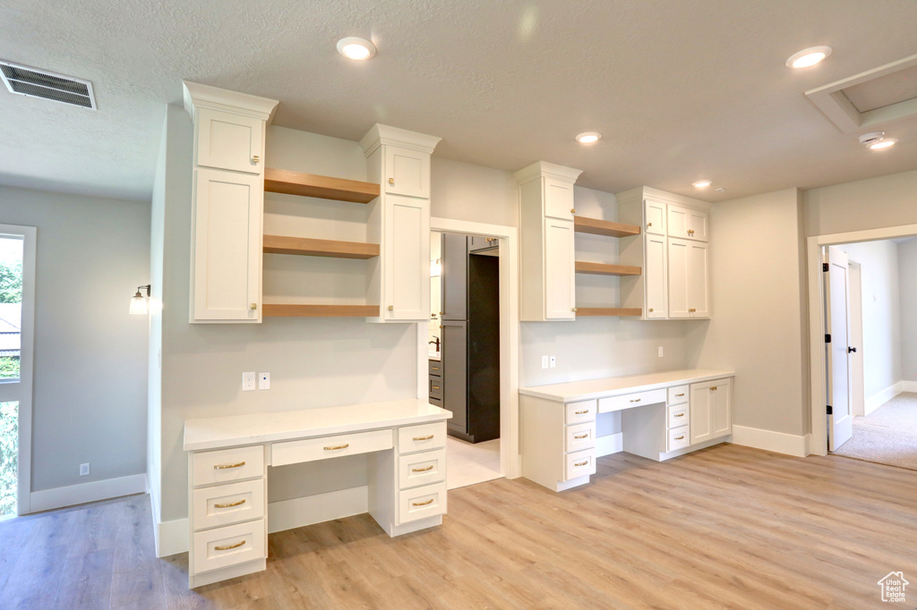 Kitchen with open shelves, built in desk, white cabinetry, light countertops, and recessed lighting