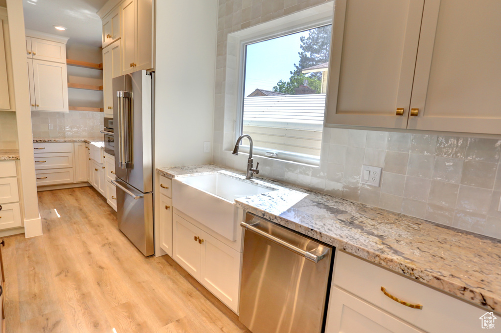 Kitchen with appliances with stainless steel finishes, backsplash, light wood-style floors, light stone counters, and white cabinetry
