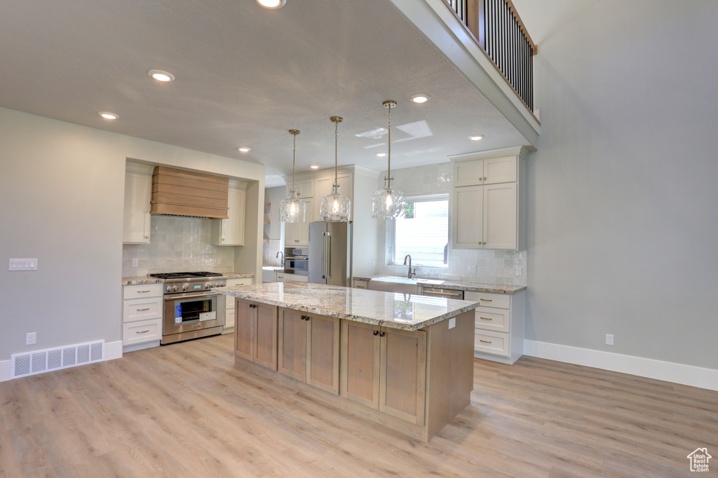 Kitchen with premium appliances, backsplash, recessed lighting, a center island, and light wood-style floors