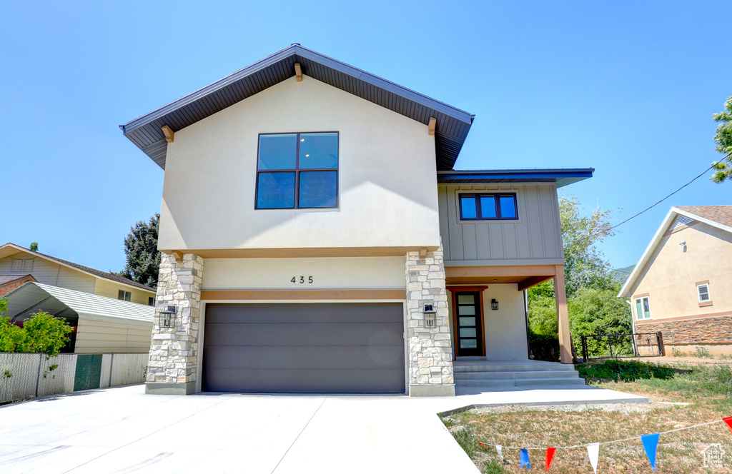 Contemporary home featuring an attached garage, driveway, stucco siding, stone siding, and board and batten siding