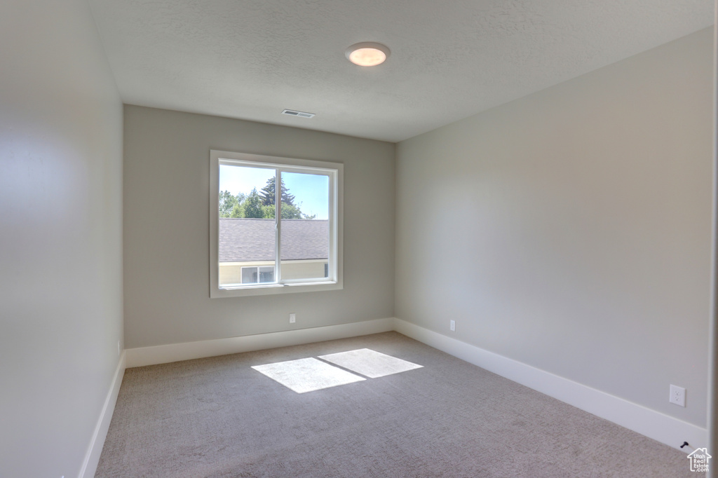 Empty room with light carpet and a textured ceiling