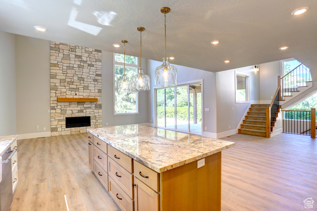 Kitchen with open floor plan, light wood-style floors, light stone counters, a skylight, and a center island