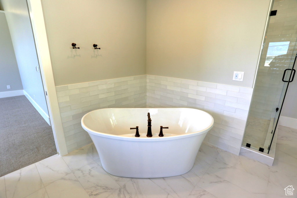Bathroom featuring tile walls, marble finish flooring, a stall shower, a soaking tub, and a wainscoted wall