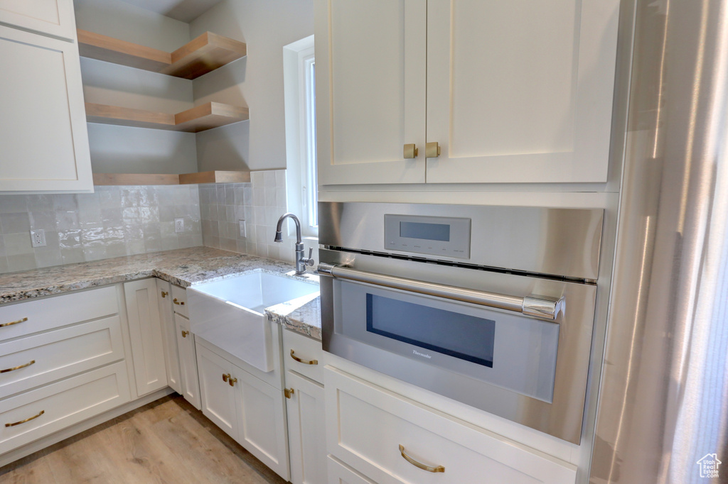 Kitchen with open shelves, stainless steel oven, white cabinets, and decorative backsplash