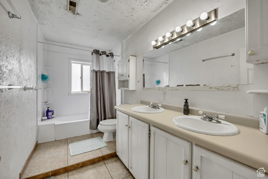 Full bathroom featuring double vanity, shower / bath combination with curtain, tile patterned floors, and a textured ceiling