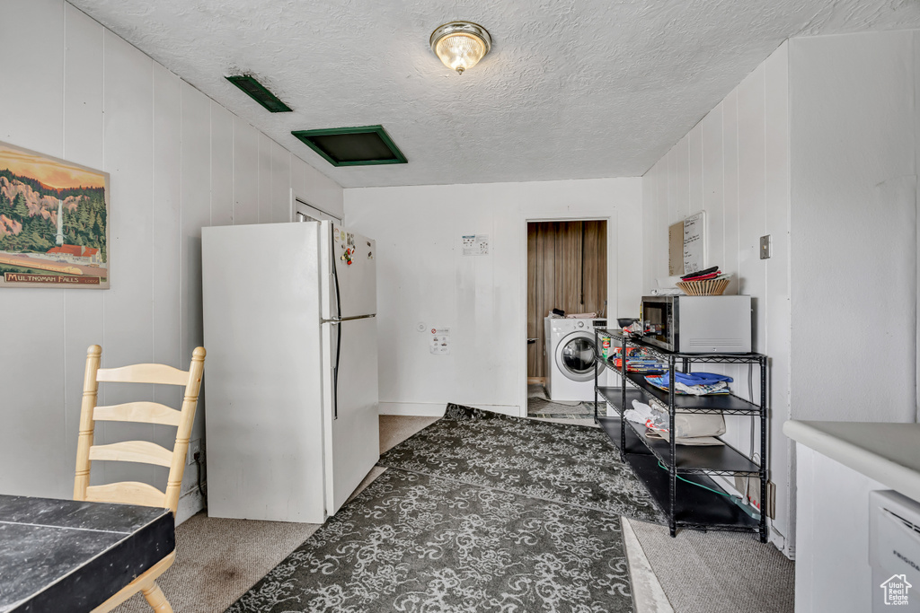 Kitchen featuring freestanding refrigerator, washer / clothes dryer, stainless steel microwave, carpet floors, and a textured ceiling