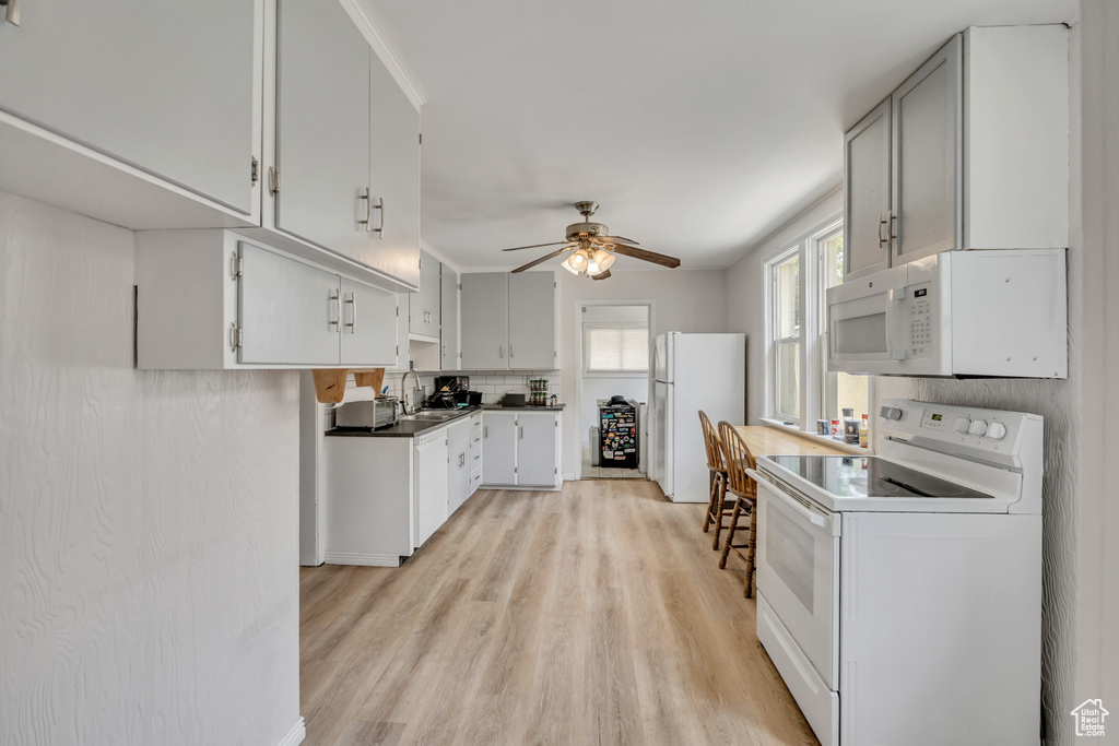 Kitchen with white appliances, light wood-type flooring, a ceiling fan, backsplash, and dark countertops