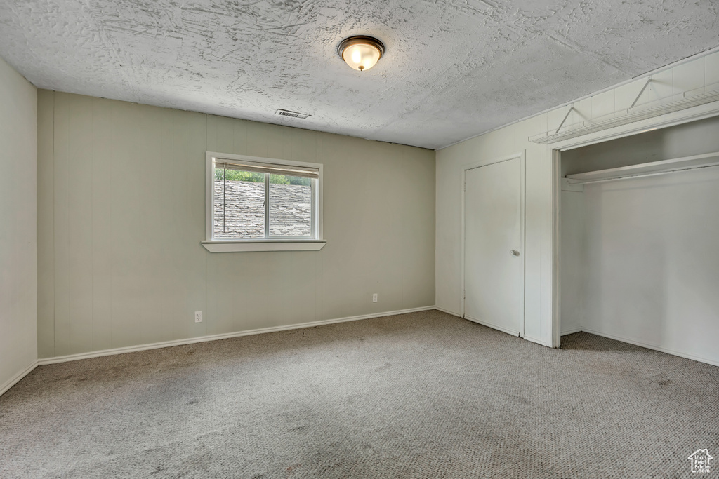 Unfurnished bedroom featuring carpet flooring, a textured ceiling, and a closet