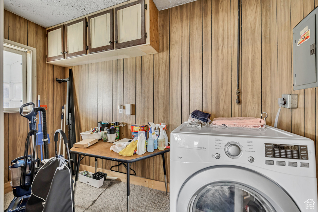 Laundry room with washer / dryer, cabinet space, wooden walls, electric panel, and a textured ceiling